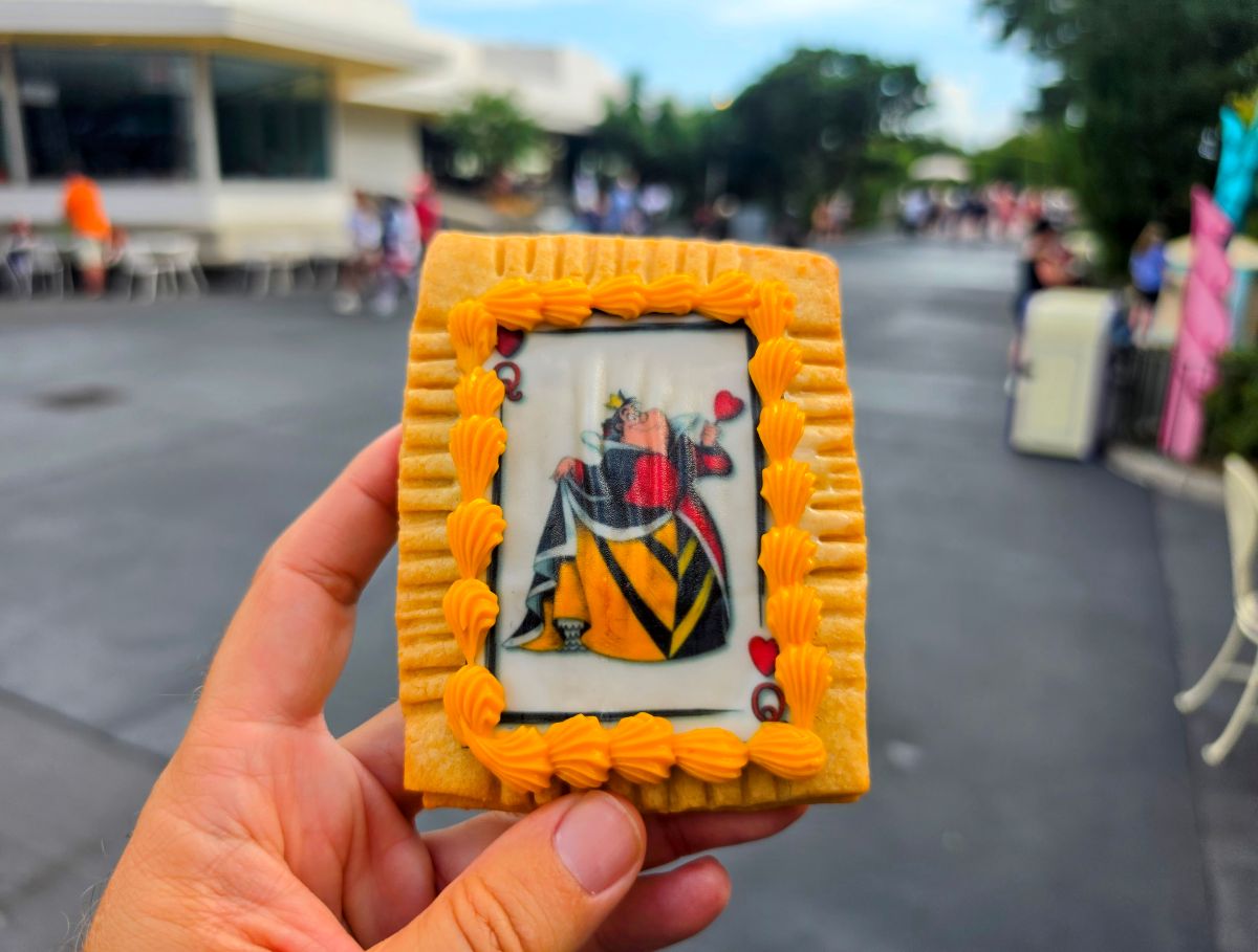 Hand holding a Queen of Hearts Tart in Magic Kingdom with pathways and park walkways in the background.