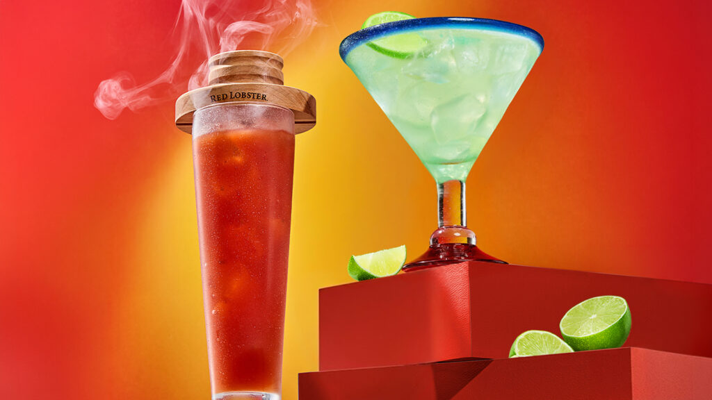 Red Lobster specialty cocktails including a smoked red cocktail in a branded glass and a blue-rimmed green margarita.