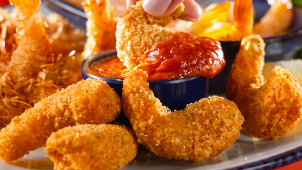 Close-up of crispy breaded shrimp being dipped into marinara sauce on a Red Lobster plate as 
Endless Shrimp returns.