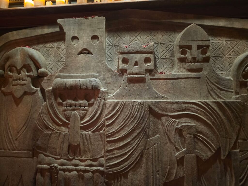 Close-up view of a carved stone wall relief depicting stylized skeleton figures wearing robes and hoods inside Six Ravens at Disney Springs.