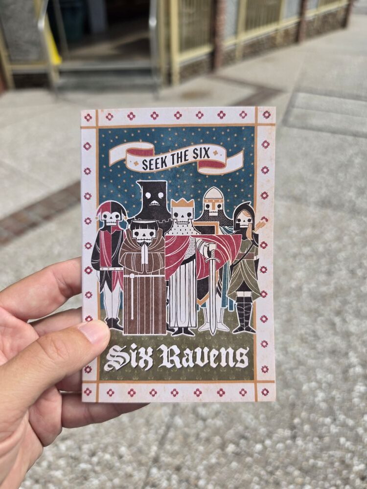 Hand holding the front cover of the Six Ravens menu featuring illustrated medieval skeleton characters under the text "Seek the Six."