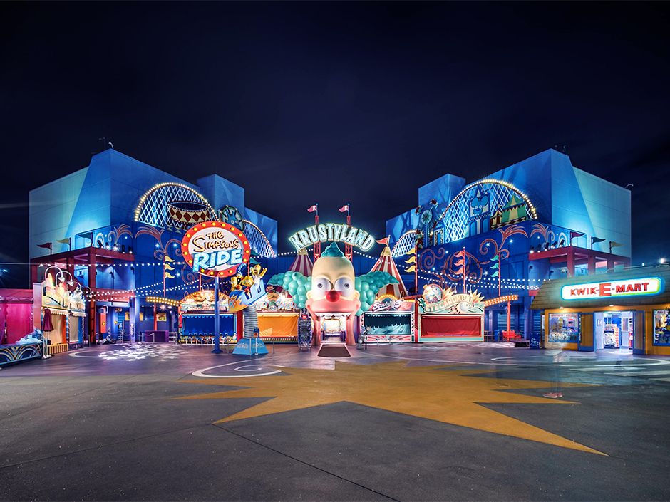 Exterior entrance to The Simpsons Ride in Krustyland at Universal Studios illuminated at night.