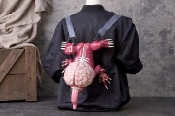 A mannequin wears a black jacket with a unique backpack shaped like a pink, brain-headed creature with a long tongue, hanging against a gray wall for the Resident Evil popcorn bucket coming to Universal Studios Japan