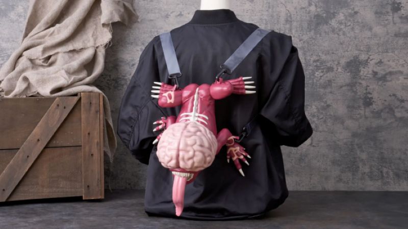 A mannequin wears a black jacket with a unique backpack shaped like a pink, brain-headed creature with a long tongue, hanging against a gray wall for the Resident Evil popcorn bucket coming to Universal Studios Japan