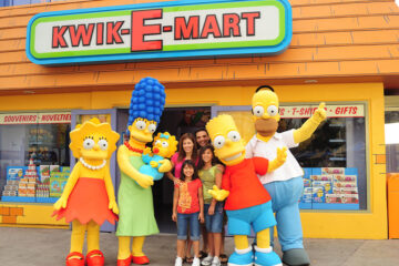 A family taking a photo with costumed characters of The Simpsons family outside the Kwik-E-Mart store.