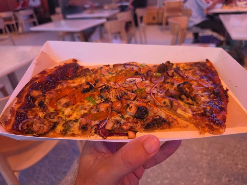 lternate view of two slices of BBQ Braai Chicken Pizza served in a white paper boat at Connections Eatery in Epcot.