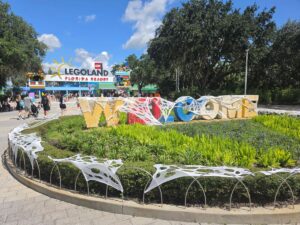Cobweb-draped Legoland Florida entrance display with large block letters spelling WELCOME surrounded by greenery during the Brick or Treat event.