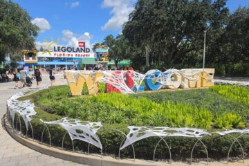 Cobweb-draped Legoland Florida entrance display with large block letters spelling WELCOME surrounded by greenery during the Brick or Treat event.