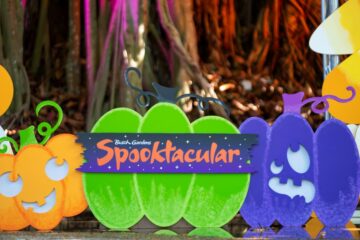 Colorful cutouts of orange, green, and purple pumpkins with carved faces, featuring a Busch Gardens Halloween Spooktacular sign in front of a wooded background.