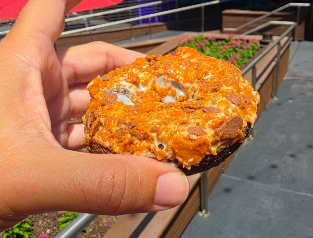 Hand holding a Butterfinger doughnut from Voodoo Doughnut at Universal CityWalk Orlando, showing crunchy topping