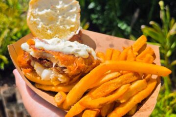 Open-faced crispy fish sandwich topped with tartar sauce alongside french fries served in a paper basket at Waterstone Grill in Aquatica Orlando.