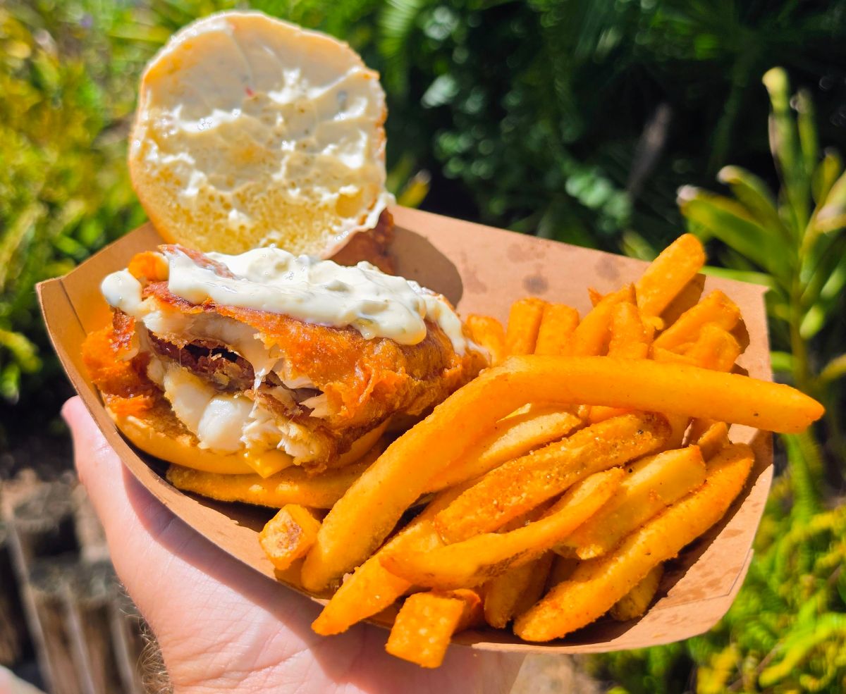 Open-faced crispy fish sandwich topped with tartar sauce alongside french fries served in a paper basket at Waterstone Grill in Aquatica Orlando.