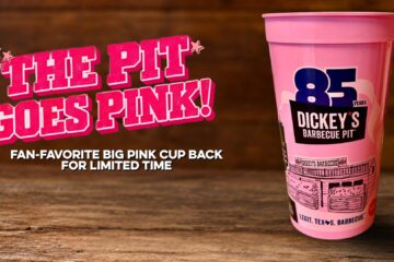 A pink plastic cup from Dickey's Barbecue Pit featuring an 85th anniversary logo and a building illustration on a rustic wooden table background.