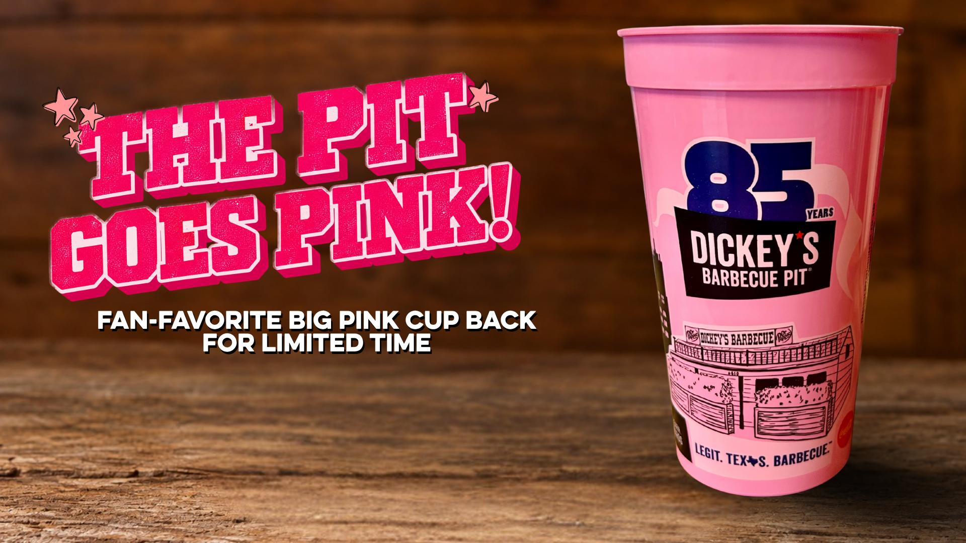 A pink plastic cup from Dickey's Barbecue Pit featuring an 85th anniversary logo and a building illustration on a rustic wooden table background.