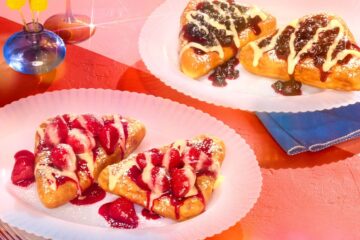 Two white plates hold IHOP Stuffed French Toast topped with strawberry or blueberry sauce and cream, set on a red surface with a blue napkin and flowers.
