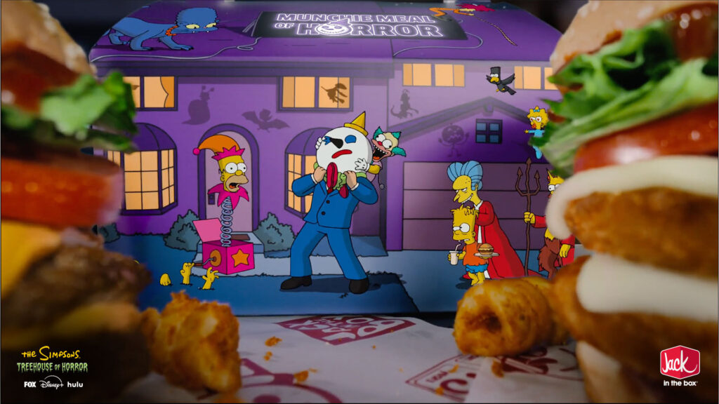 A purple Jack in the Box Munchie Meal of Horror box featuring Simpsons characters, flanked by two burgers and fried snacks on a branded paper liner.