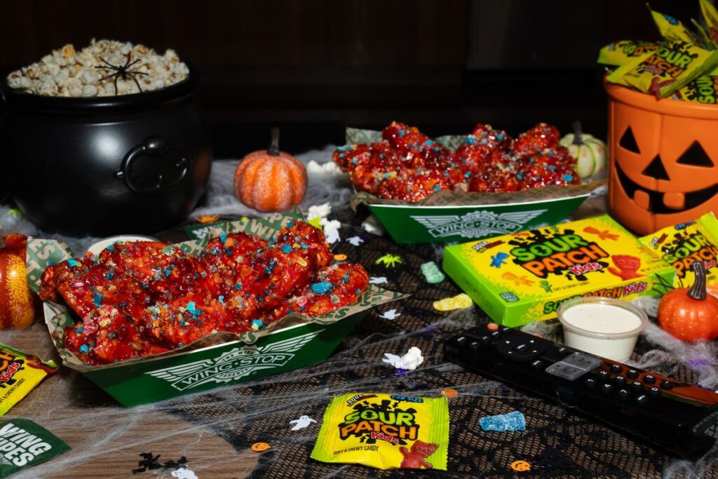 Wingstop chicken wings topped with Sour Patch Kids candy, served with popcorn in a cauldron, a jack-o'-lantern, and candy on a spooky table.